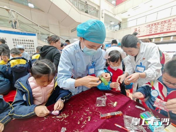 医护人员让现场40名小学生体验挑选艾叶、藿香等药材，并动手制作中药香囊的过程。