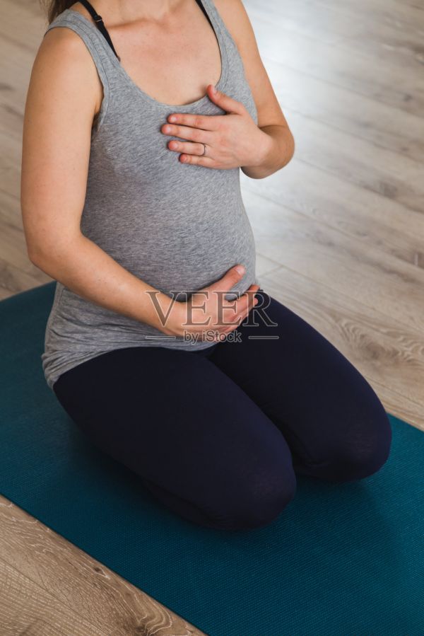 孕妇跪在瑜伽垫上，双手放在心脏和腹部做产前瑜伽照片摄影图片