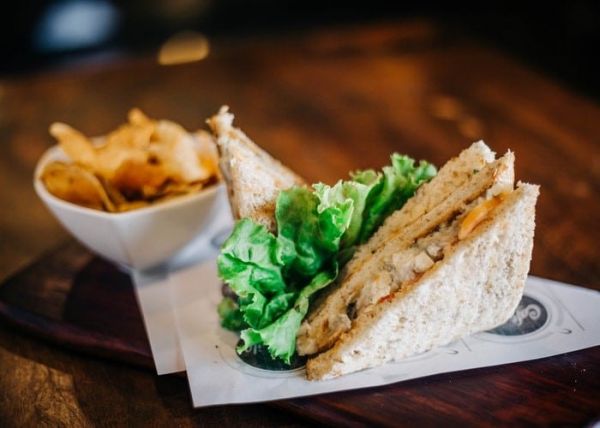 Un bocadillo de pollo con hojas verdes y patatas fritas