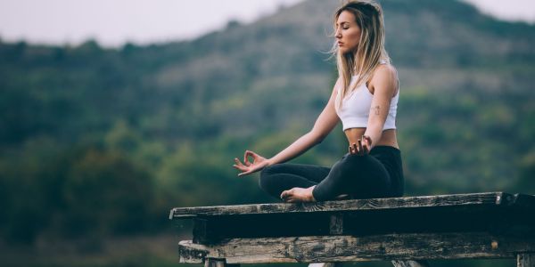 Young woman meditating outdoors on a wooden platform, practicing mindfulness for natural calm and relaxation in a serene natural setting.