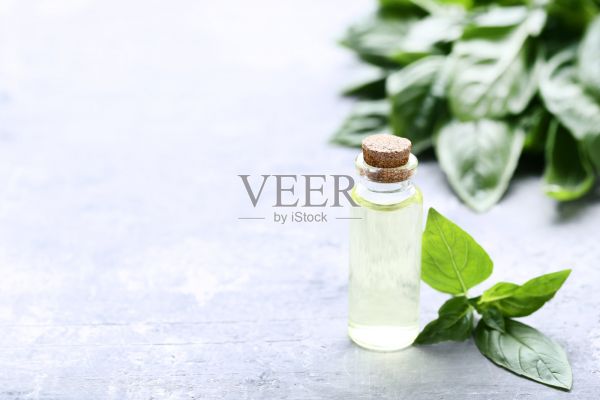 灰色的木桌上放著一瓶精油和羅勒葉照片攝影圖片