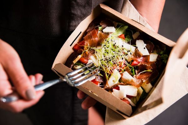 woman's hand is holding a take away fresh salad in a lunch box