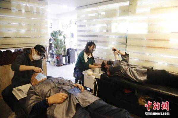 资料图：市民佩戴口罩来到理发店理发，店员佩戴口罩进行服务。中新社记者 马铭言 摄