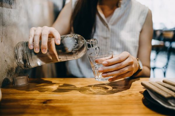 midsection of young asian woman pouring water from bottle into the glass in a restaurant