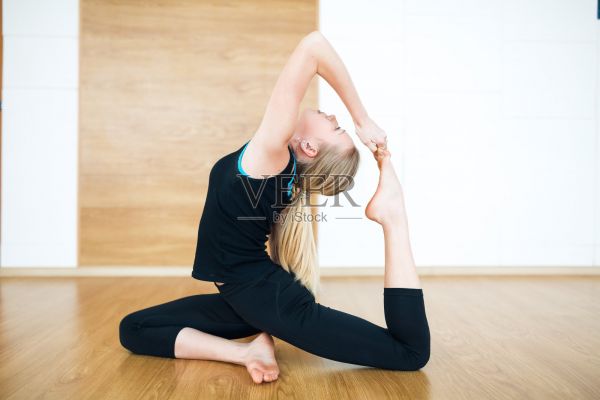年輕的金發(fā)女人在一個(gè)黑色套裝做哈他瑜伽體式Eka pada rajakapotasana -一只腿的國(guó)王鴿子在瑜伽墊子上的瑜伽墊子在健身房照片攝影圖片