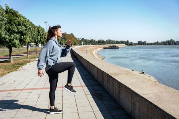 young strong sexy muscular fit woman in doing high knee skip running in the place as hard outdoor workout training in the autumn cold and sunny weather as preparation for marathon race