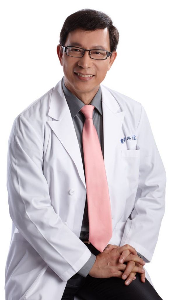 a healthcare professional wearing a white lab coat and pink tie seated with hands clasped