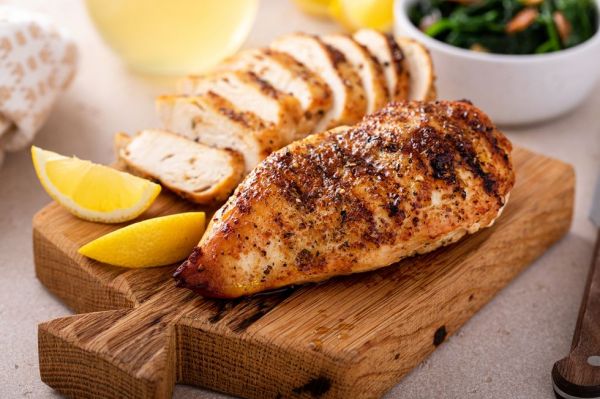grilled chicken breast whole and sliced on a cutting board with lemon