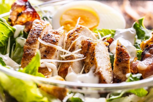 delicious caesar salad with grilled chicken slices in a glass bowl