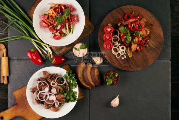 深色的石头背景上放着三个盘子。新鲜低卡路里沙拉，健康小吃，主菜。配料蘑菇，番茄，洋葱，胡萝卜，大蒜，胡椒，鸡胸肉，绿色香料。照片摄影图片