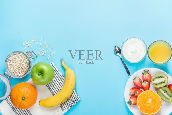 健康早餐配料燕麥蘋果香蕉草莓獼猴桃橙子酸奶汁勺子在藍(lán)色的桌面上?？瞻啄Ｐ蛷?fù)制空間的文本。平面構(gòu)成。膳食計(jì)劃照片攝影圖片