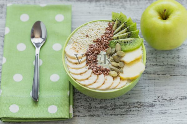 绿色冰沙碗，上面有猕猴桃，香蕉，苹果和种子，这是健康的纯素食早餐照片摄影图片