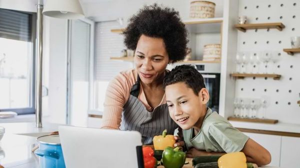 Young boy and his mother in the kitchen preparing food from a recipe on a tablet