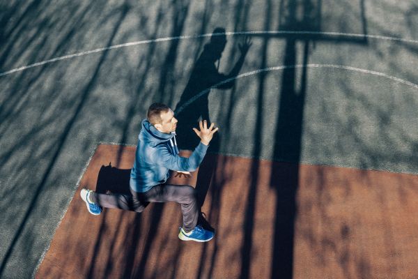 A man improving his cardiovascular endurance by doing a workout outside. He's in a lunge.