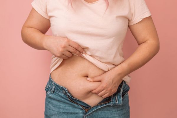 woman hand holding excessive belly fat, overweight concept overweight female wearing a jeans