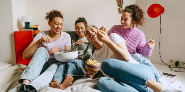 cheerful female friends watching tv while enjoying snacks at home