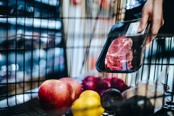 close up of woman pushing a shopping trolley, grocery shopping for fresh poultry in supermarket she is putting a packet of steak into the shopping cart routine grocery shopping healthy eating lifestyle