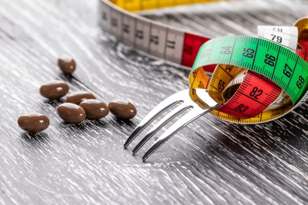 a shiny fork wrapped in a multi colored centimeter to measure body shapes and brown medical capsules