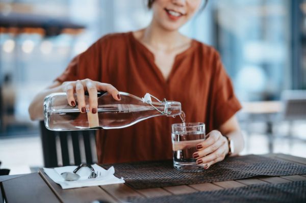 young asian woman pouring water from bottle into the glass at outdoor restaurant healthy lifestyle and stay hydrated