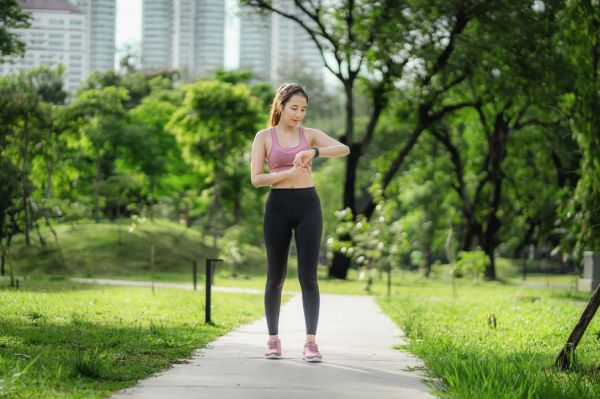 beautiful asian runner looks at her smart watch in a park after jogging to check if health is still in good shape or not concept of urban society and health care