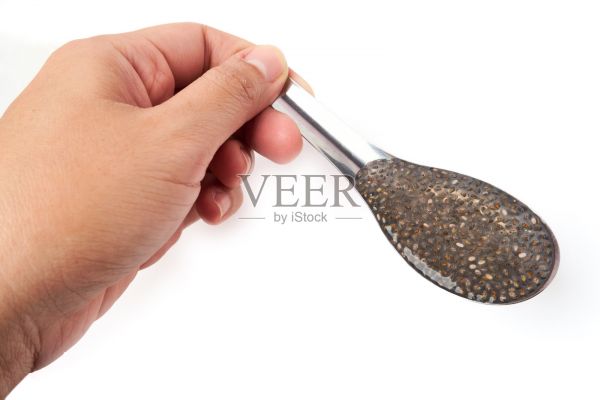 汉德手里拿着一个盛着奇亚籽的勺子，这些奇亚籽浸泡在白色背景的水中后膨胀起来。含有omega-3，蛋白质，纤维和维生素。照片摄影图片