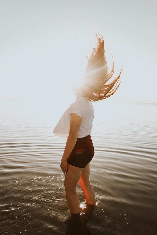 Woman standing in sea with sun behind her.