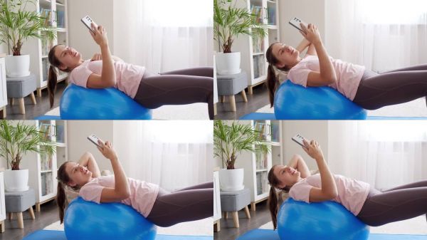 年轻女子用智能手机拍摄健身训练和健身球运动的视频。运动、健身和瑜伽博主和有影响力的人。