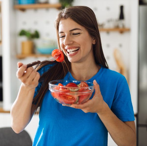 smiling woman eating salad in the kitchen