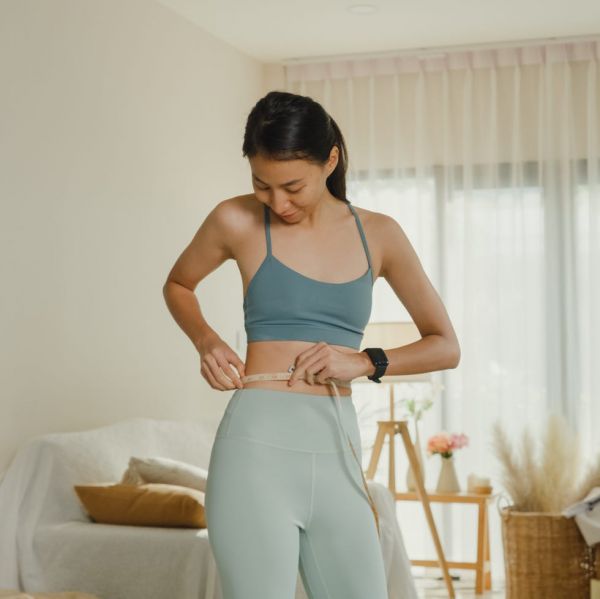 young asian athletic woman with a tape measure body perfect slim weight loss in front of a mirror in living room at home diet and healthy weight loss