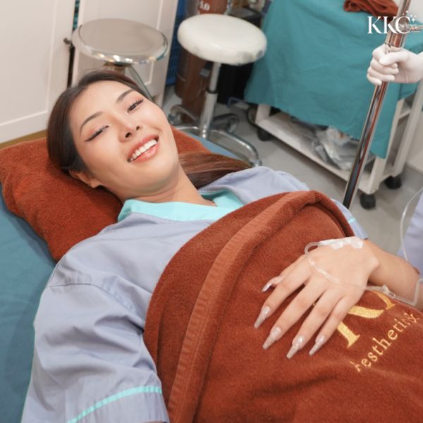 ผู้ป่วยที่ KKC Clinic กำลังนอนยิ้มอยู่บนเตียงรักษาและรับการให้สารทางหลอดเลือด พร้อมกับห่มผ้าห่มสีน้ำตาล