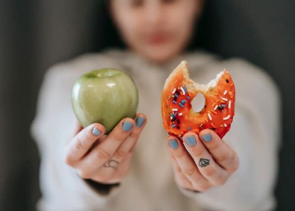 Una mujer decidiendo si come una manzana o un donut