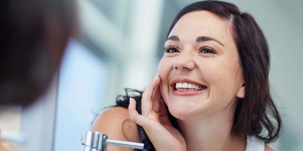 Smiling woman looking at her reflection in a mirror, showcasing clear and radiant skin, representing natural solutions for achieving a healthier complexion.