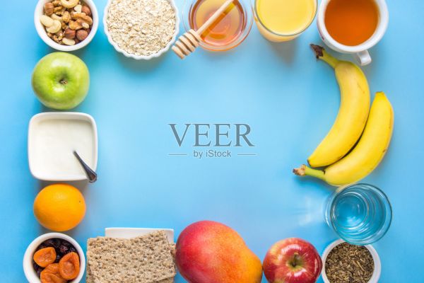 健康早餐食物纤维来源燕麦蜂蜜水果苹果香蕉橙汁水绿茶坚果。蓝色的桌面。现代时髦的平面Lay框架鲜艳的颜色俯视图。海报及横幅版面照片摄影图片