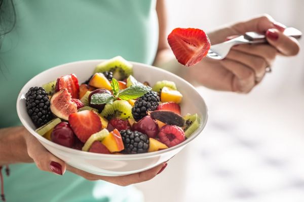 a woman breakfasts a fruit salad high in vitamins and fiber.