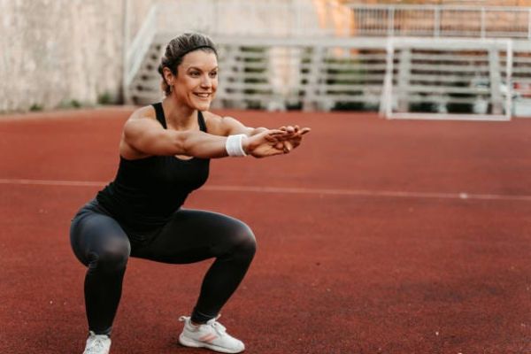 beautiful young woman doing squats on a running track
