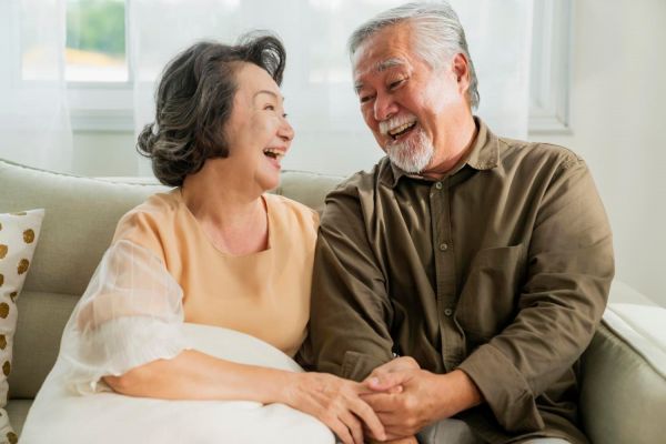 兩位年長夫婦坐在沙發(fā)上愉快地交談並大笑，展現(xiàn)出健康與幸福的生活狀態(tài)。