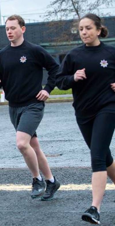 Firefighters in fitness gear running on concrete with an appliance in the background