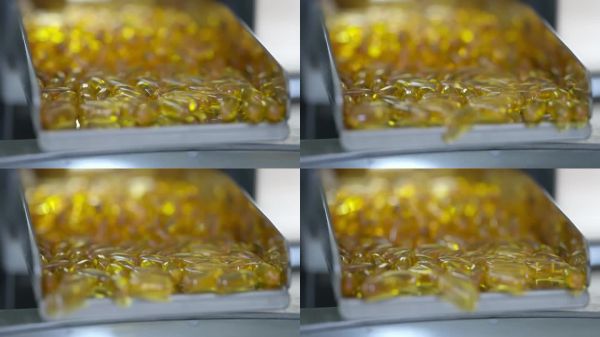 许多黄色明胶鱼油维生素D3 Omega 3药用胶囊药片从高处掉落。制药工厂的自动生产线设备。药物在输