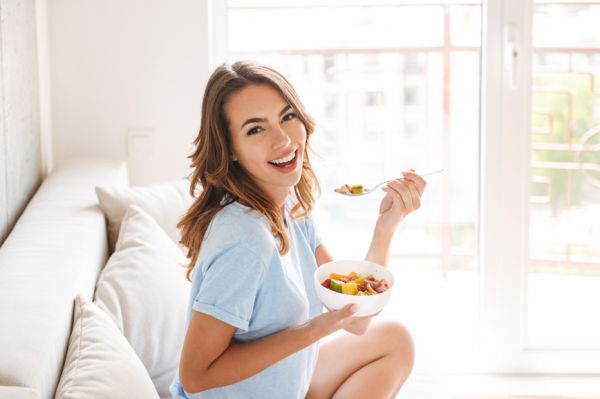 女性がサラダを食べながら笑顔でソファーに座っている