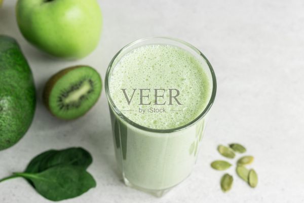綠色排毒奶昔，混合素食飲料，蛋白質(zhì)奶昔在一個(gè)杯子里的菠菜，蘋(píng)果，鱷梨，獼猴桃和種子在一個(gè)桌子上，健康的飲食理念照片攝影圖片