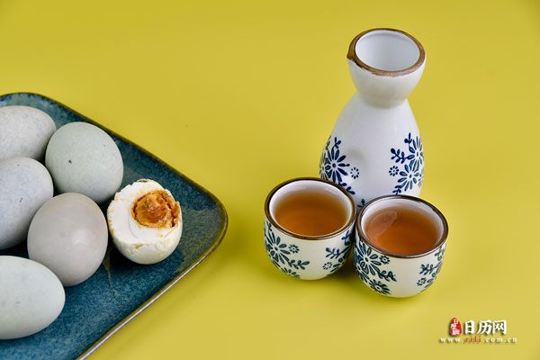 黄色背景下盘子里的熟咸鸭蛋雄黄酒-