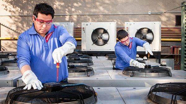 Two men repairing air conditioning units, focused on their work in a well-lit mechanical space.