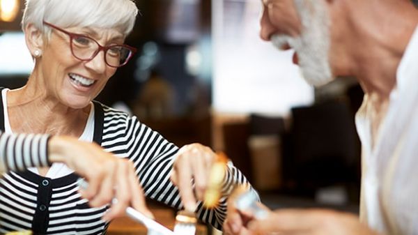 An older couple enjoys a meal together at a cozy restaurant, smiling and engaged in conversation.