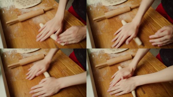 青少年用手揉面團(tuán)，形成光滑的圓柱形。桌子上撒滿了面粉，以便于操作。搟面杖靜靜地放在旁邊，準(zhǔn)備進(jìn)行下一