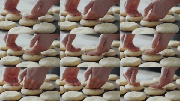 特寫鏡頭：熟練的雙手輕柔地按壓和塑形生面團，準備烘焙自制的扁面包或漢堡包。