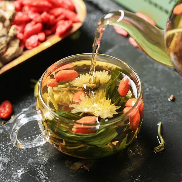 一杯沖泡中的玫瑰花枸杞茶，透明玻璃杯中漂浮著紅色枸杞和粉色干玫瑰花瓣，熱水升騰起裊裊熱氣，背景為木質(zhì)茶桌與自然光線