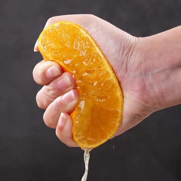 一位成年人正在用刀將橙子切成兩半，手部動作清晰，桌面整潔，旁邊放有砧板和完整橙子