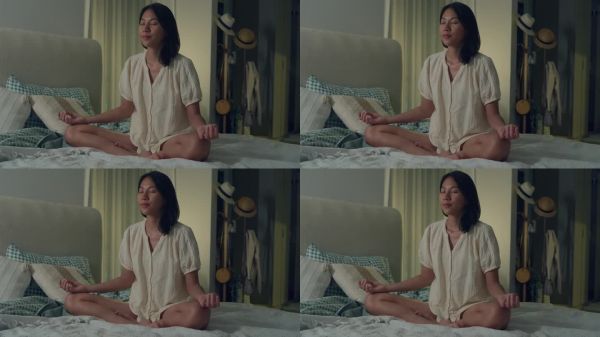 年轻的亚洲女人穿着睡衣，她躺在床上，咒语冥想，晚上在家里的卧室里手拉手做瑜伽。日常的生活方式。