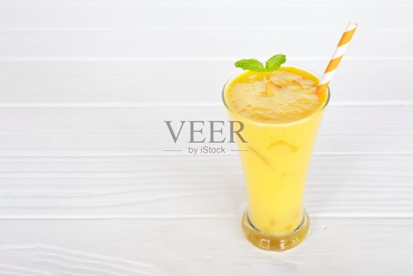 芒果冰沙黄色彩色果汁奶昔混合饮料健康高蛋白味道美味在玻璃饮料减肥饮料情节早上在白色木制背景。照片摄影图片