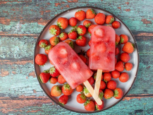 2 strawberry popsicles along with fresh strawberries on a plate